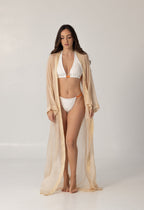 Woman wearing a white and orange bikini with a sheer beige cover-up standing against a plain background showcasing the ISAURA luxury swimwear style.