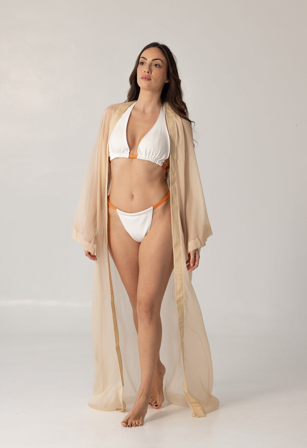 Model wearing ISAURA white and orange bikini paired with a sheer beige beach cape, showcasing elegant and luxurious resort wear style.