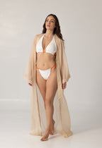 Model wearing ISAURA white and orange bikini paired with a sheer beige beach cape, showcasing elegant and luxurious resort wear style.